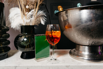 Chilled Aperitif Drink and Elegant Decor. An orange aperitif in a wine glass on a chic bar counter,...