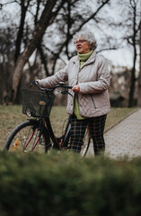 Mature female retiree standing with her bicycle, looking at the distance in a tranquil park setting.