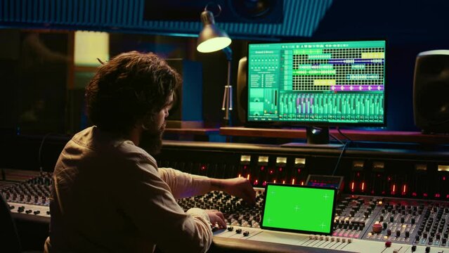 Audio technician working with music recording software and editing tunes, mixing console and control panel board in post production studio. Producer operating technical equipment. Camera B.