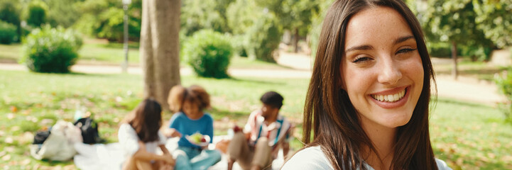 Close-up of young smiling woman with long brown hair posing for the camera in the park, Panorama....