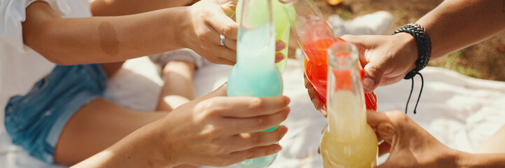 Close-up of hands raising toasts, with drinks in their hands, colorful drinks at picnic on summer...