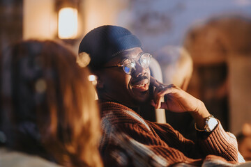 Stylish man in glasses enjoying conversation in a cozy evening setting.