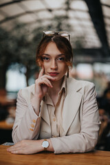 A poised young professional woman sits at a table, her thoughtful gaze suggesting confidence and strategy in a business environment.