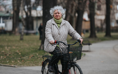 An active senior woman with curly hair holds onto her bicycle in a serene park setting, exuding health and contentment.