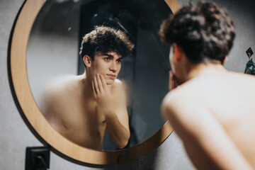 Bare-chested young adult examining himself in the mirror with a contemplative expression