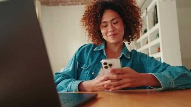 Smiling young woman looking at mobile phone in living room