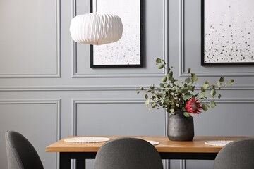 Soft chairs, table and vase with plants in stylish dining room