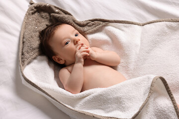 Cute little baby in hooded towel after bathing on bed, top view