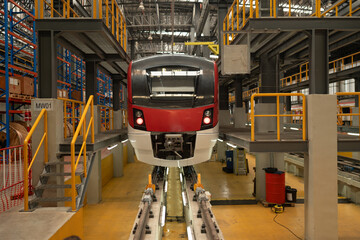 Front view of a red and white modern train situated on tracks in a maintenance depot, with...