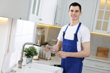 Smiling plumber repairing faucet with spanner in kitchen - obrazy, fototapety, plakaty