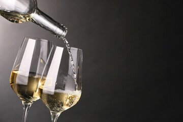 Pouring white wine into glass against grey background, closeup. Space for text