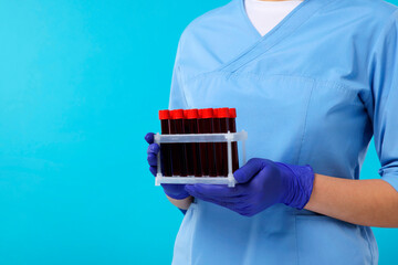 Laboratory testing. Doctor with blood samples in tubes on light blue background, closeup. Space for...