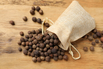 Aromatic allspice pepper grains and sack on wooden table, top view