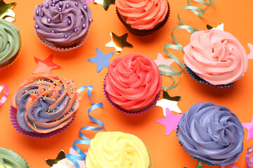 Delicious cupcakes with bright cream and party decor on orange background, flat lay