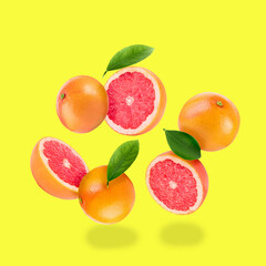 Fresh ripe grapefruits and green leaves falling on yellow background - obrazy, fototapety, plakaty
