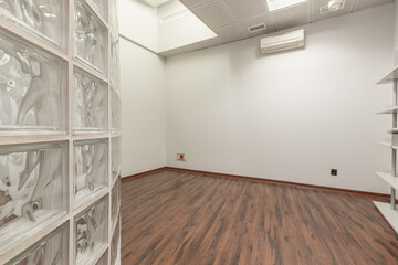 An empty office with a wooden bookshelf and a glass paves brick wall