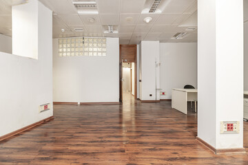 An empty office with several pillars, a desk between them, dark wooden doors, a dividing wall,...