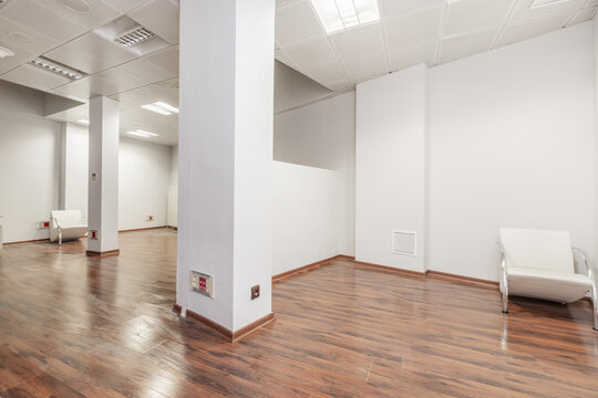 An empty office with several pillars, a dividing wall, plain white walls and a reddish floor
