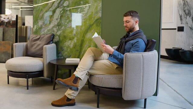 Handsome man chooses tiles on the catalog in luxury shop
