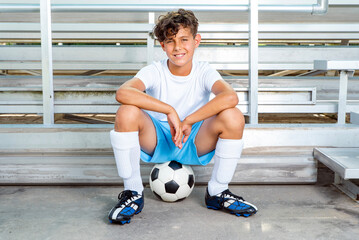 Smiling young male soccer player sitting on a soccer ball happy after winning a game