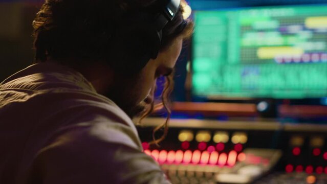 Young composer songwriter recording his guitar tunes in professional studio, composing new music on mixing console and daw software. Artist musician singing new tracks in control room. Camera A.