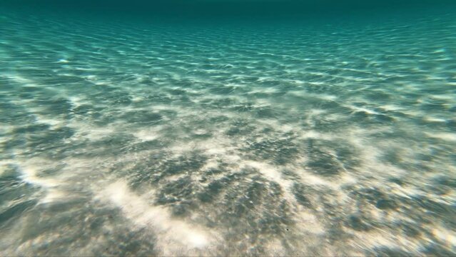 Slow motion underwater video of sunlight waves playing on the white sandy bottom at the turquoise shallow water of Elafonissi Beach. Crete. Greece