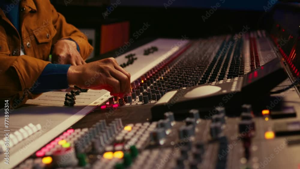 Poster African american producer uses control desk with automatic equalizer, mixer and sliders to edit tracks in post production. Sound engineer processing audio recordings, mixing console. Camera B.