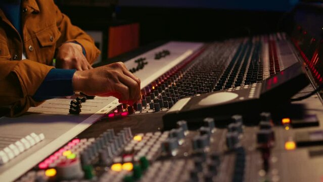 African american producer uses control desk with automatic equalizer, mixer and sliders to edit tracks in post production. Sound engineer processing audio recordings, mixing console. Camera B.