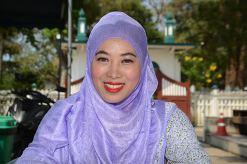 Face of young Asian woman wearing hijab sitting and posing in a park.
