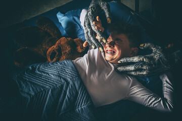 Terrified young boy in bed at night attacked by a scary monster