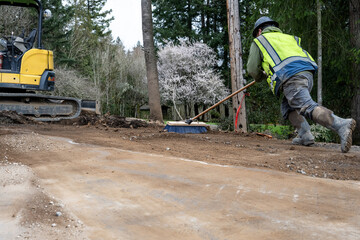 Construction worker with push broom cleaning dirt off road from stump removal during a road construction project
