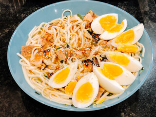 Spaghetti with chicken pieces, herbs, sesame seeds, egg. An appetizing breakfast on a round plate.  Idea for restaurant menu or advertisement 