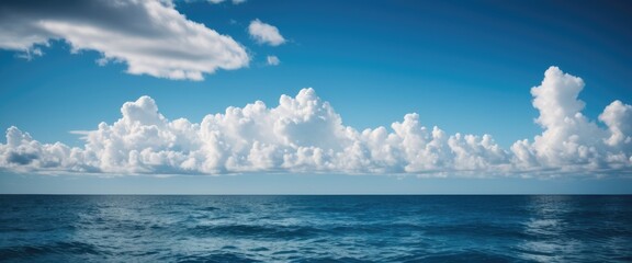 Capture the serene expanse of a blue sky with fluffy clouds drifting over the ocean - obrazy, fototapety, plakaty