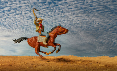A cowboy galloping fast with his horse.  Miniature HO scale figurine.