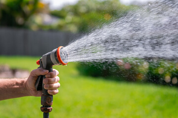 Garden hose with nozzle. Man's hand holding spray gun and watering plants, spraying water on grass...