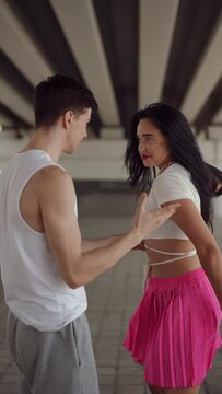 Vertical video. The guy stands under the bridge and waits. Furious girl with long black hair runs up to the guy, grabs his hands and backhands him in the face, running away