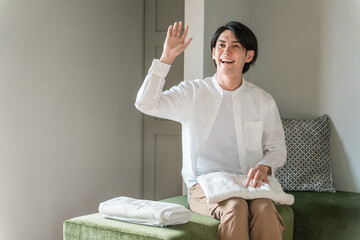 タオルを畳みながら手を振る笑顔の主婦（おかえりなさい・新婚・挨拶）
