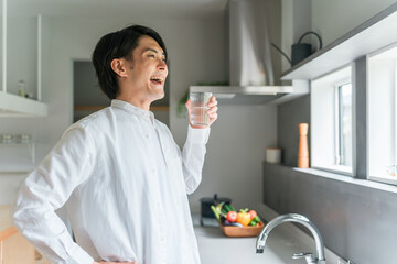 キッチンで水・白湯を飲む若いアジア人男性（水分補給・温活）

