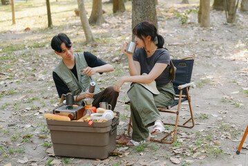 Asian couple clinking coffee mug together at camp side, They feeling relaxed and refreshing while camping in the nature. Recreation