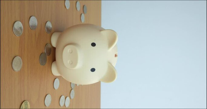 hand releases coin into piggy bank, capturing the essence of money. Against scattered coins, it's visual metaphor for money management. Money, both saved and spent is depicted vividly. Vertical video.