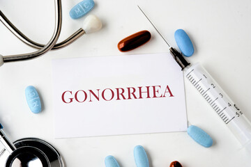 GONORRHEA word on the card near the stethoscope, pills, syringe on a white background - obrazy, fototapety, plakaty