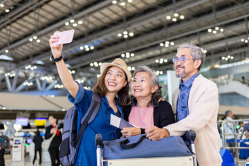 Group of Asian family tourist passengers with senior is using mobile phone to take selfie photo at airport terminal during vacation travel and long weekend holiday