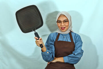 beautiful Asian woman in brown apron, glasses and hijab hold pan while doing housework. smile...
