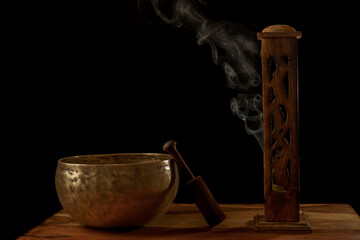 Tibetan singing bowl next to a wooden censer with smoke coming out isolated on black background...