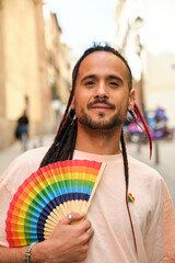 Gay man with a rainbow fan smiling and looking at camera at International Pride Day.