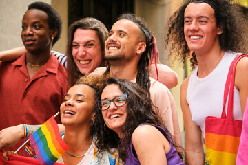 A group of people are smiling and holding rainbow flags. They are all friends and are posing for a...