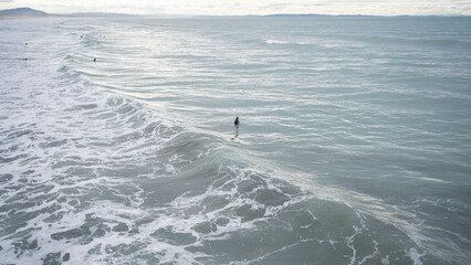 Fototapeta premium Surfers in rough ocean water waiting to catch approaching waves, New Zealand