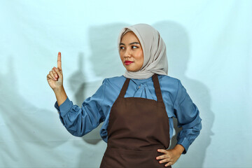 unhappy young Asian Muslim woman in hijab and brown apron showing stop gesture refusing say no...