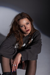 Glamorous beautiful woman in a fashion sweatshirt sitting and looking at the camera in the studio on a dark background
