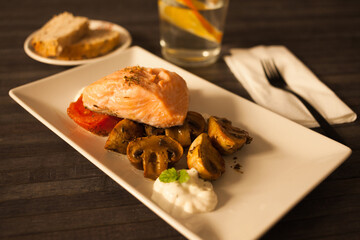 Steamed salmon fillet on a pillow of fried mushrooms and tomatoes on a white plate